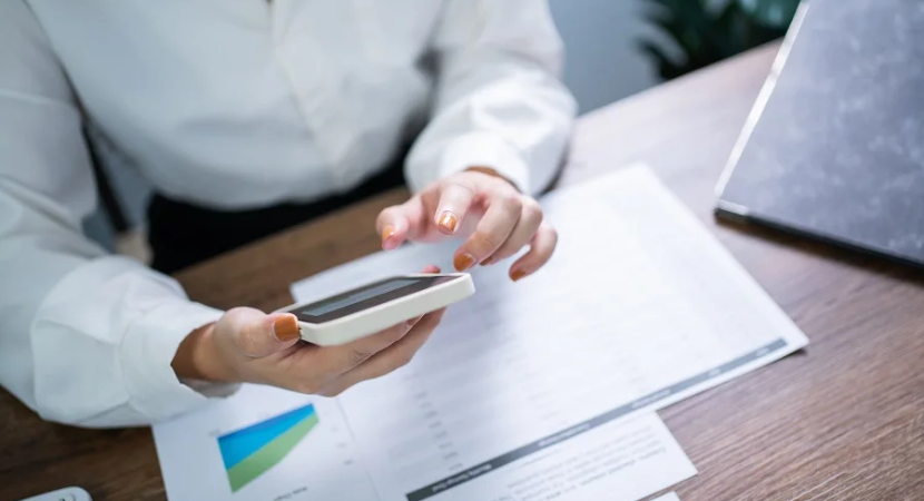 Woman holding a phone over a table with documents.